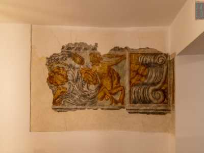 Raffigura un satiro con ai piedi la testa di un drago, tra decori vegetali e volute